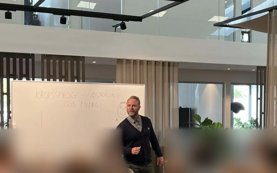 Jesper Bergstrøm foran en whiteboardtavle med teksten Kropssprog, udstråling og god energi under et foredrag hos Dansk Motor Finans